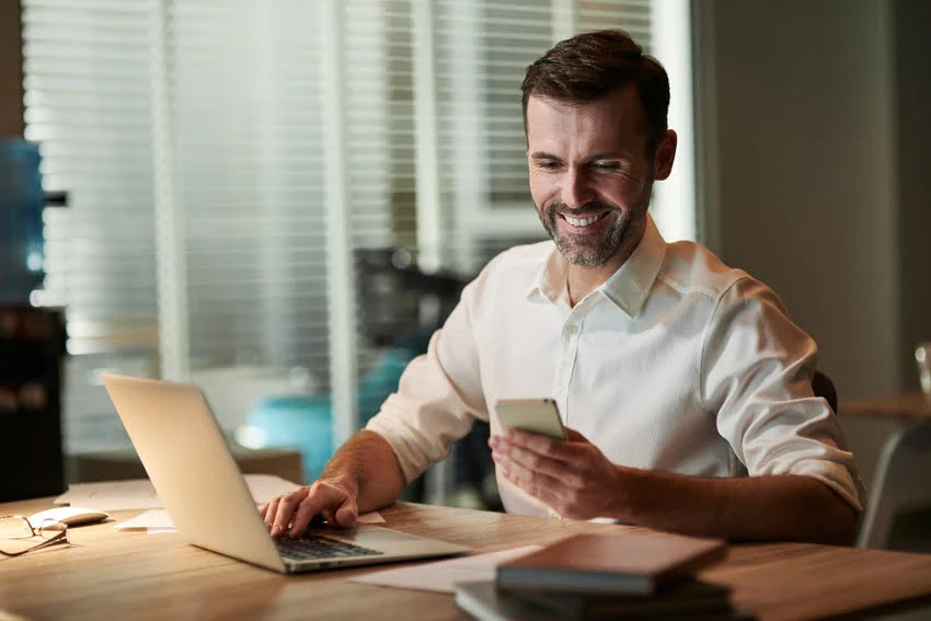 Homem Sorrindo com celular na mão sentado em um escritório